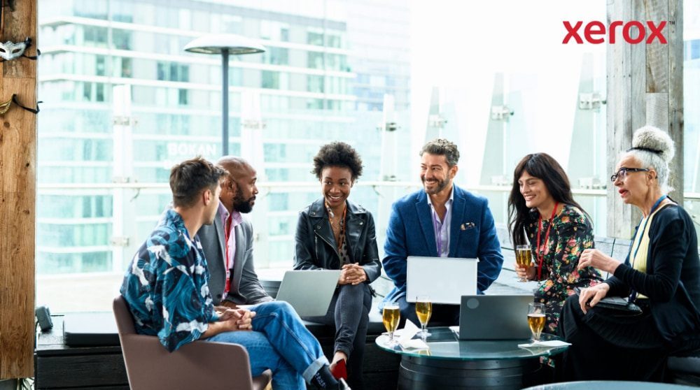 Un gruppo di sette persone sedute insieme, conversano e lavorano su laptop con una città sullo sfondo Un gruppo di sette persone sedute insieme, conversano e lavorano su laptop con una città sullo sfondo