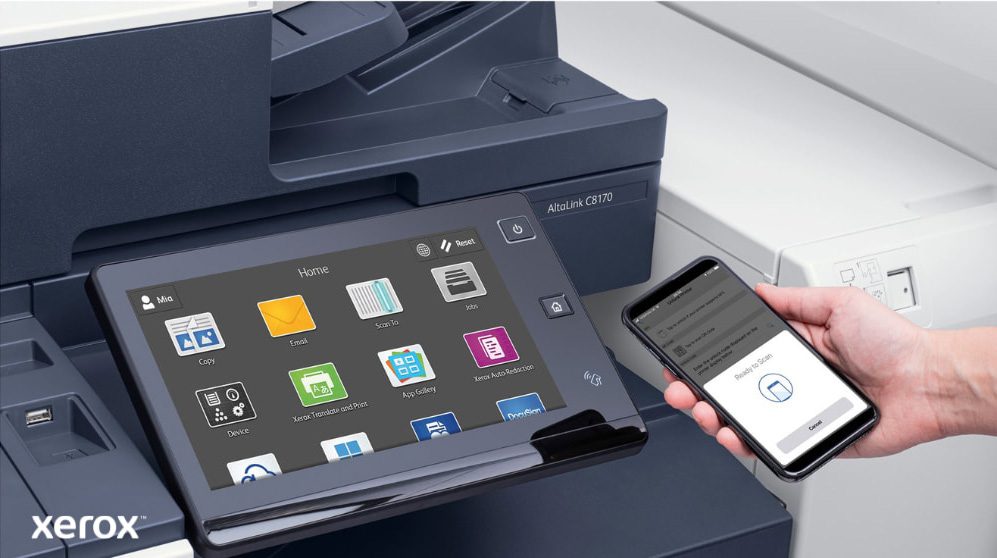 Primo piano della mano di una persona che tiene uno smartphone, connesso in modalità wireless al pannello di controllo touchscreen di una stampante multifunzione Xerox, che mette in mostra le funzionalità di stampa e scansione mobile senza interruzioni di Xerox ConnectKey.