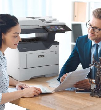 Un uomo e una donna seduti a un tavolo, impegnati in una conversazione mentre una stampante Xerox® è posizionata nelle vicinanze.