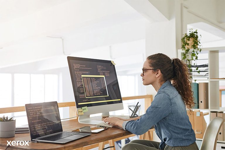 Una donna alla sua scrivania, impegnata con un computer e un laptop, dimostra produttività in uno spazio di lavoro moderno.