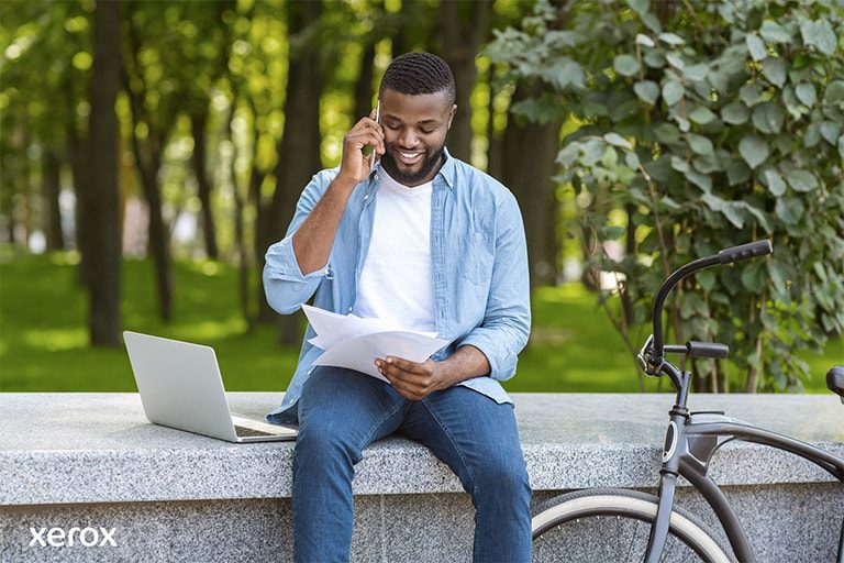 Un uomo è seduto su una panchina, usa il suo laptop, mentre la sua bicicletta è parcheggiata accanto a lui in un ambiente tranquillo.