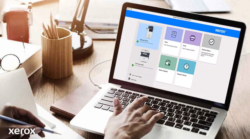 Le mani di una persona sono sulla tastiera di un computer portatile e sullo schermo viene visualizzata l'interfaccia Xerox Print and Scan Experience con opzioni quali Scansione, Stampa, Stato del dispositivo, Ordina materiali di consumo e Centro assistenza, a dimostrazione di un controllo intuitivo.