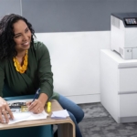 Donna sorridente in un ufficio accanto alla stampante a colori Xerox® VersaLink® C620